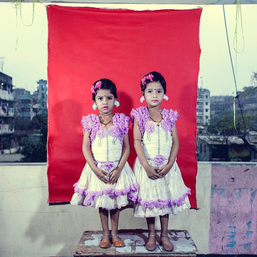 Two children in matching dresses standing against a red backdrop