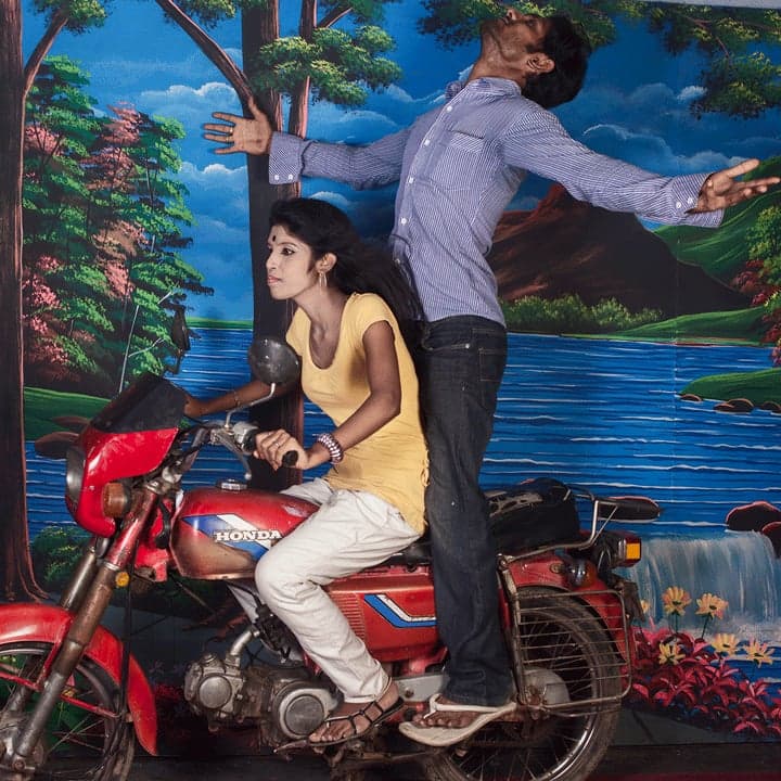 A couple posing on a red motorcycle before a painted garden